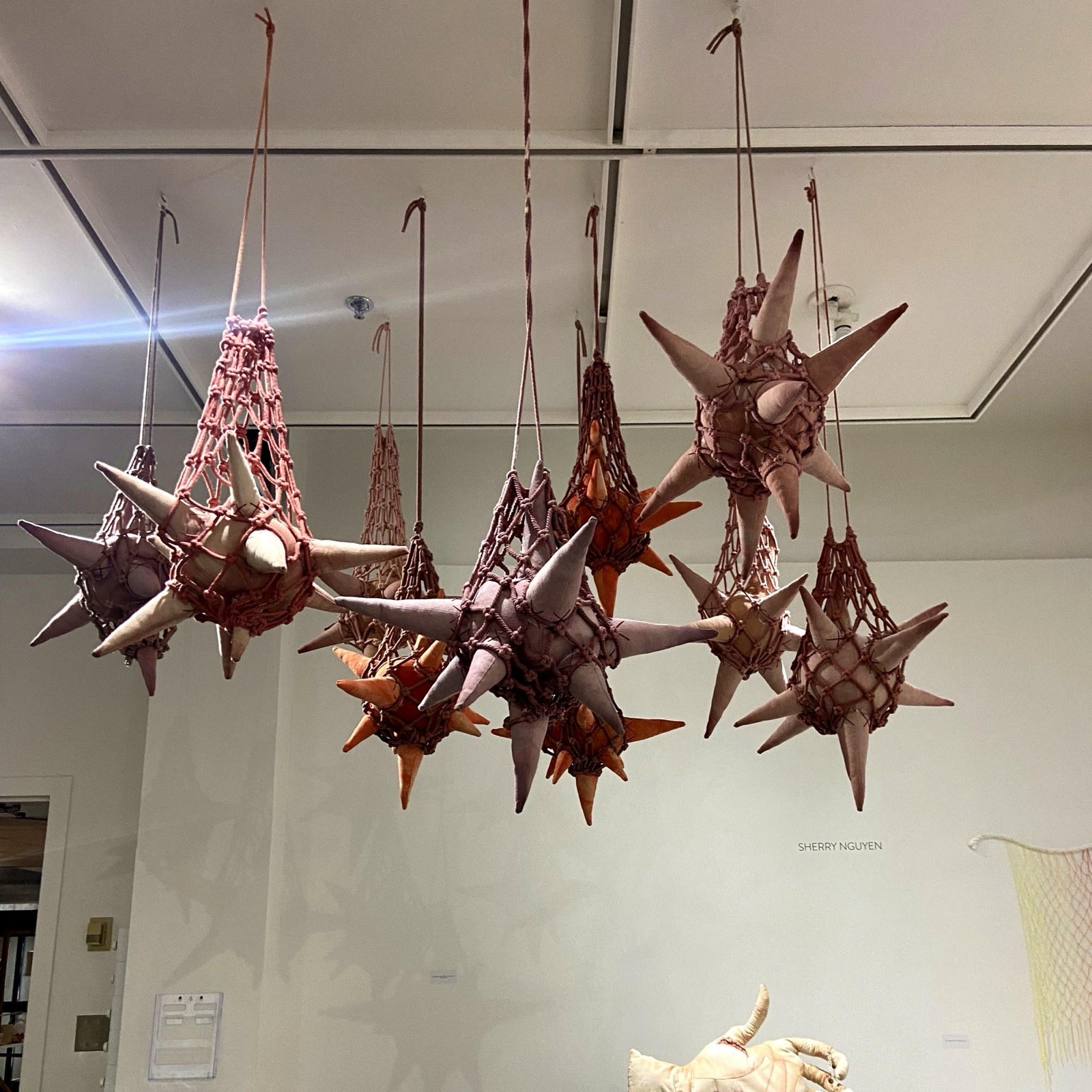 Emotional Mines — spiked soft forms in flesh-toned dyed canvas, suspended in knotted netting in a white gallery.